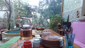 A wooden table set with plates, mugs, and a teapot in a garden with a brick wall and plants. - Lotus Garden Hostel (Izmir)