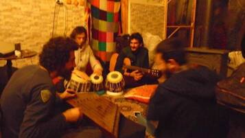 Un grupo de personas tocando instrumentos musicales tradicionales en una habitación con pared de ladrillo y ventana.