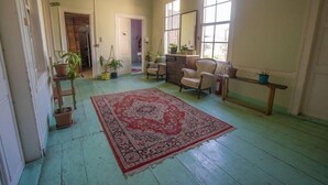 A spacious room with a large red patterned rug, wooden furniture, and several potted plants. - Lotus Garden Hostel (Izmir)