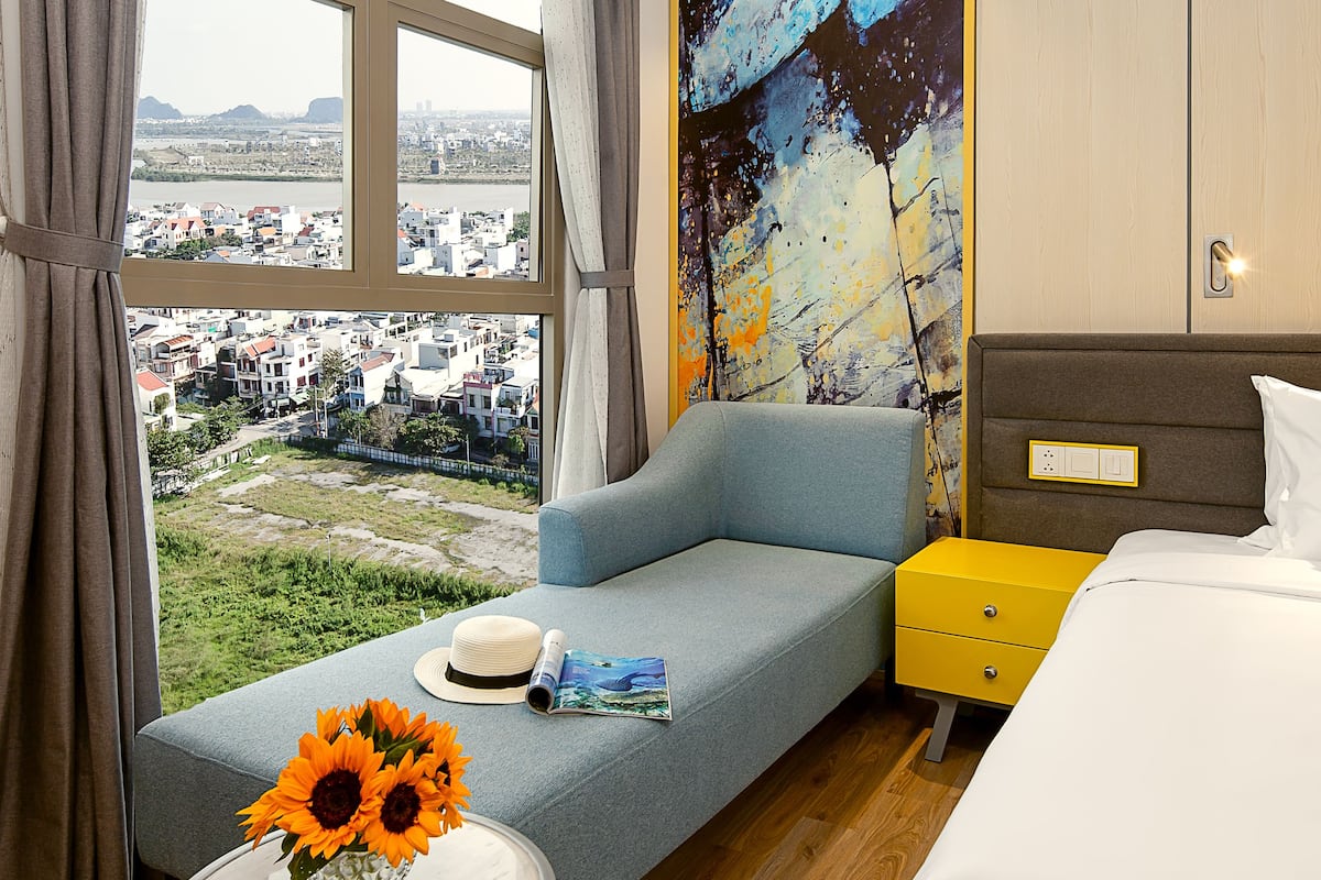 Et hotelværelse med stort vindue, sofa, seng og et lille bord med blomster.