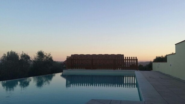 A swimming pool with a clear view of the surrounding area, including a building with a fence and trees. - Fattoria Albanese Labardi (Lastra a Signa)