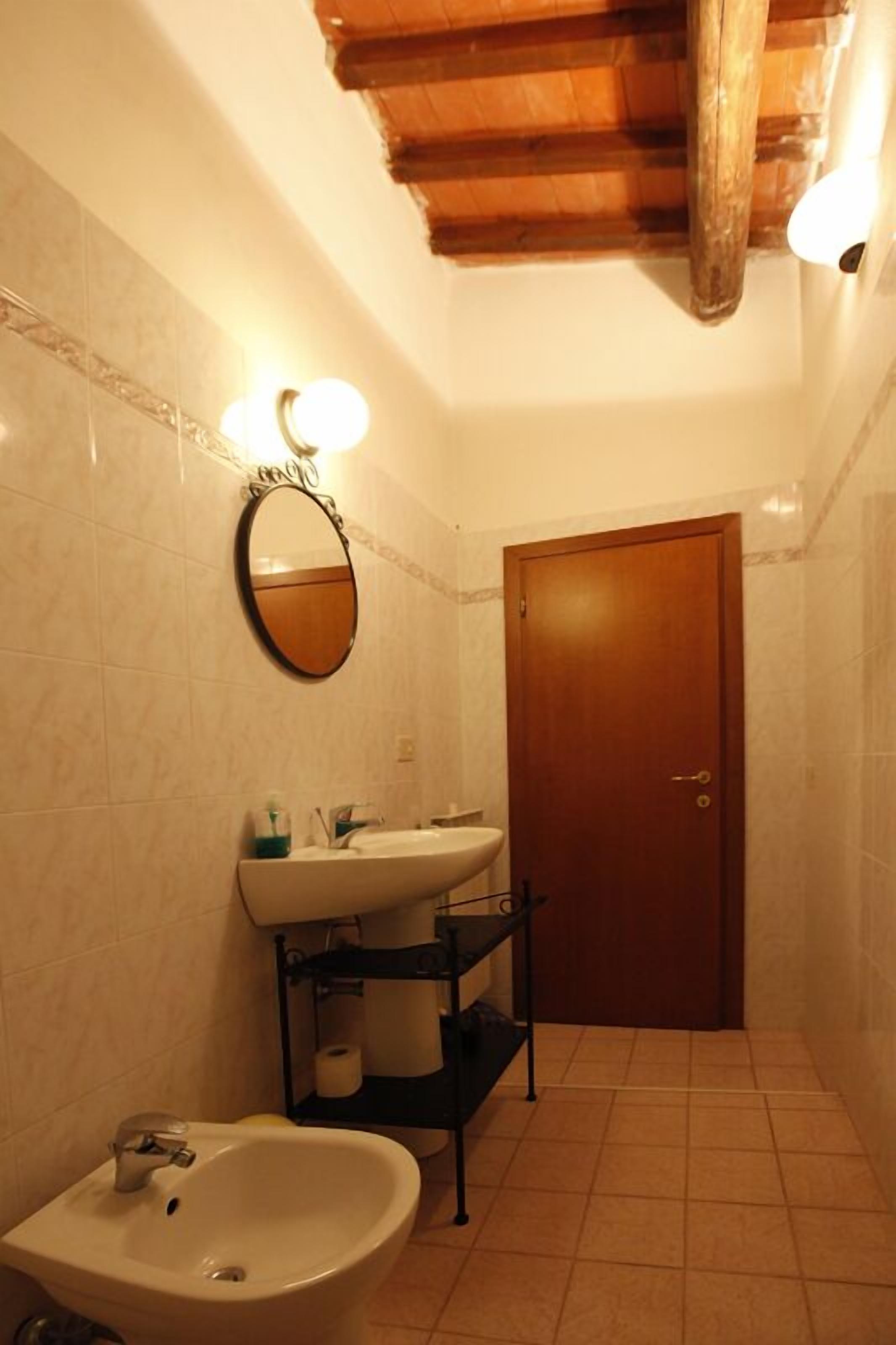 Ein Badezimmer mit Waschbecken, Bidet und Spiegel. Eine Holztür und ein Ablagebereich mit Toilettenartikeln sind ebenfalls vorhanden.