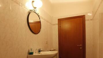 Ein Badezimmer mit Waschbecken, Bidet und Spiegel. Eine Holztür und ein Ablagebereich mit Toilettenartikeln sind ebenfalls vorhanden.