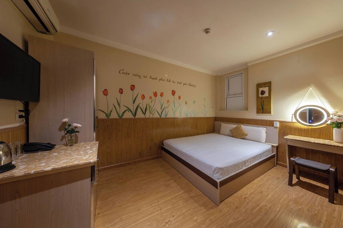 Un dormitorio con cama, mesita de noche y televisión instalada en la pared.