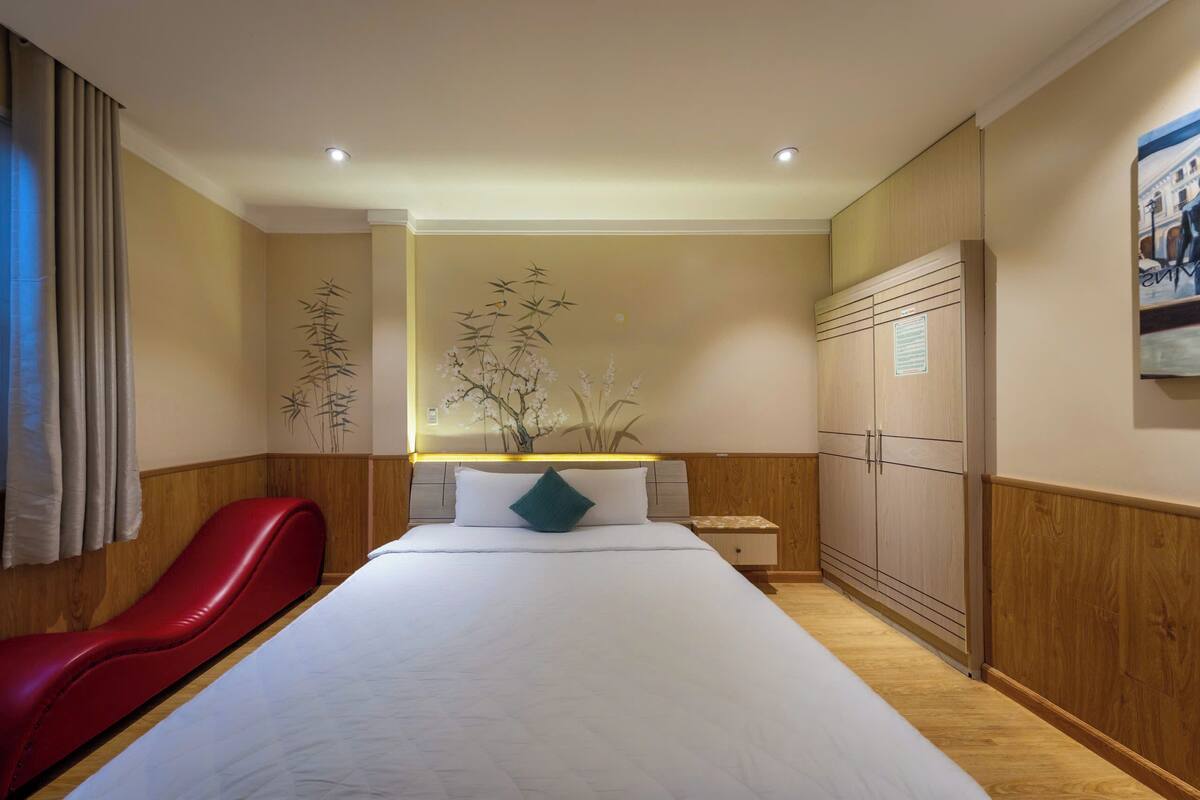 Habitación de hotel con una cama grande, una silla roja, paneles de madera, una mesita de noche y un armario.