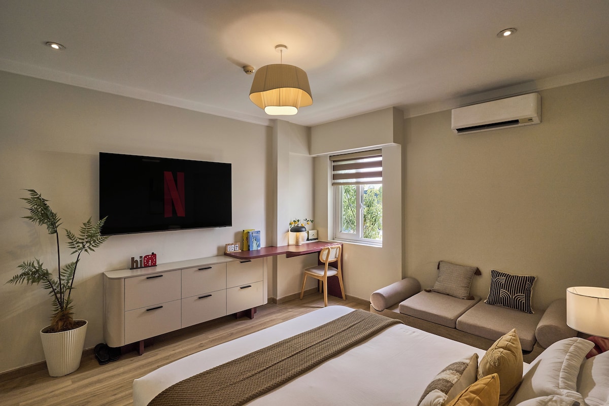 A modern bedroom with a bed, a desk, a chair, a sofa, a TV, and a potted plant.