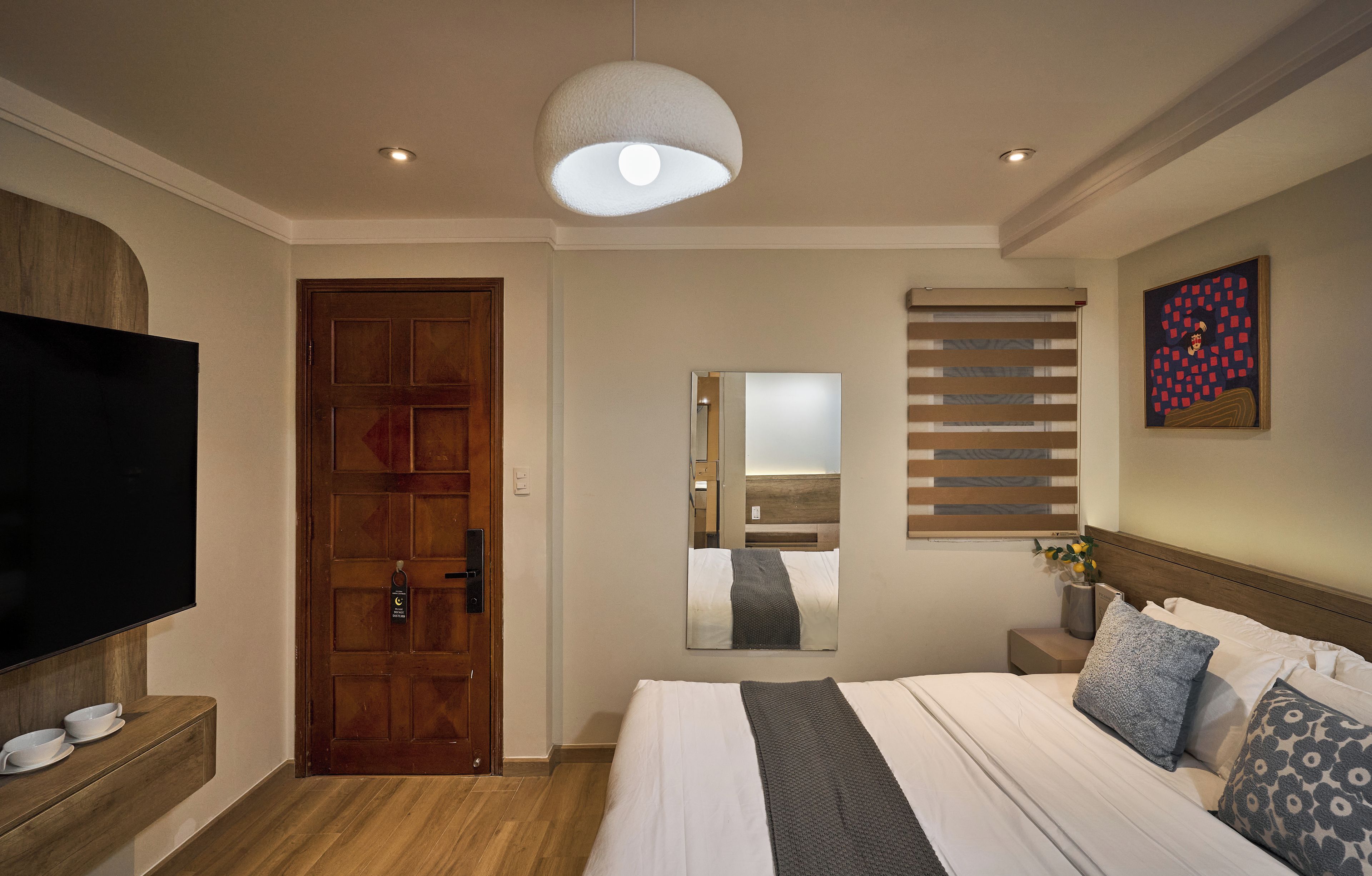A hotel room with a large bed, a television, a wooden door, and a ceiling light.