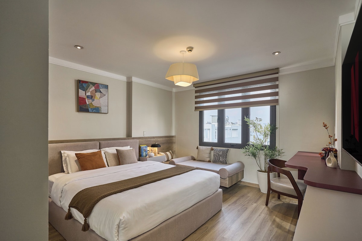 A hotel room with a bed, bedside table, lamp, window, and a view of the outside.