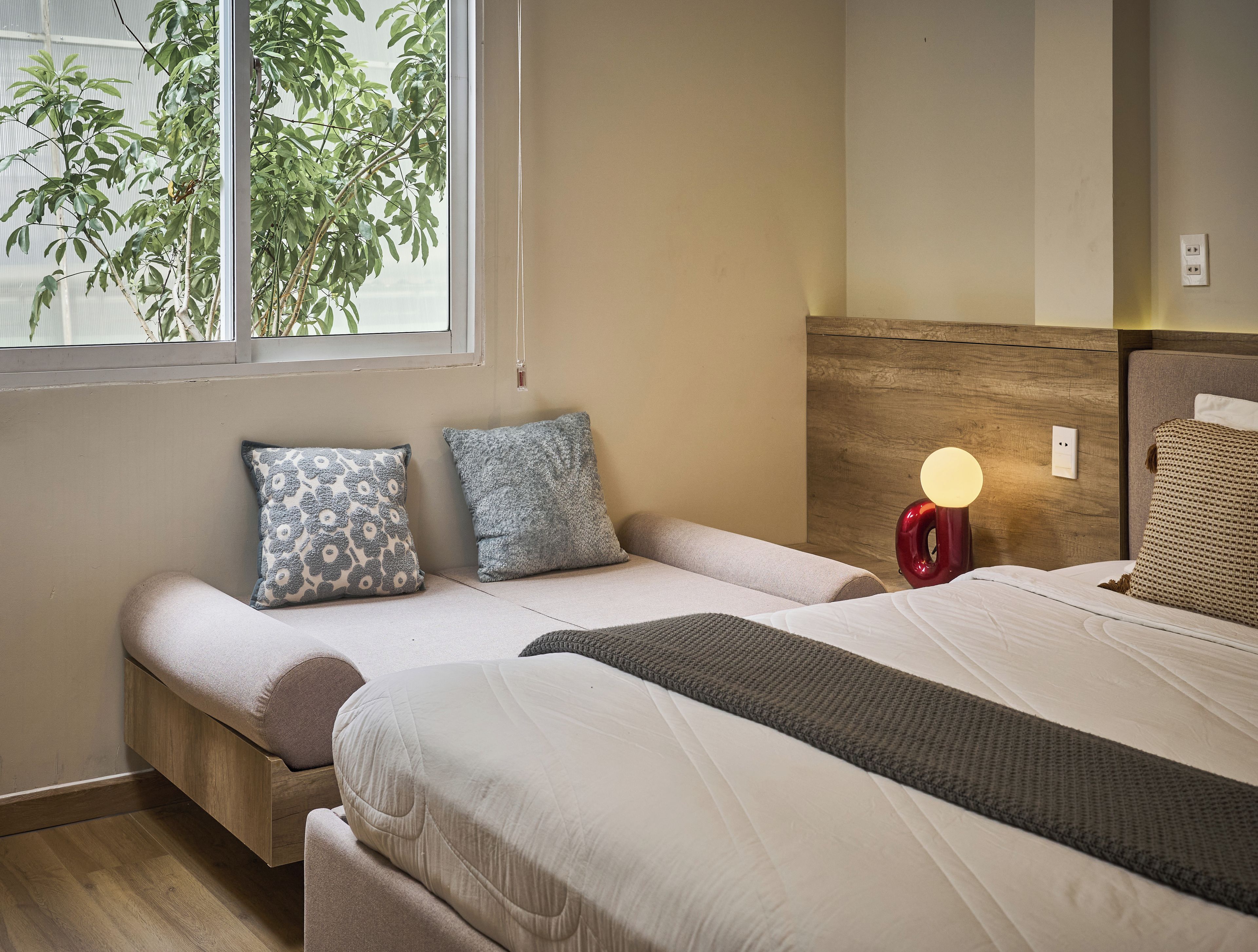 A bedroom with a bed, bedside tables, a lamp, and a window with plants.