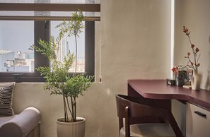 A modern room with a large window, a potted plant, a wooden desk, and a cushioned bench. - Maison Truong Thinh Hotel by Urban B (Ho Chi Minh City)
