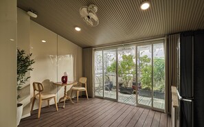 A room with a wooden floor, a table, two chairs, a potted plant, and a sliding glass door leading to an outdoor area with plants and a view of the sky. - Maison Truong Thinh Hotel by Urban B (Ho Chi Minh City)