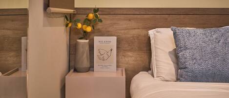 Un dormitorio ordenado con una cama, una mesita de noche con un jarrón de flores y un libro titulado 'PICASSO'.