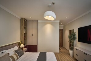 A modern bedroom with a bed, bedside table, lamp, wardrobe, and a TV mounted on the wall. - Maison Truong Thinh Hotel by Urban B (Ho Chi Minh City)