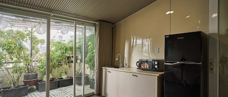 Una cocina moderna con un refrigerador negro, un microondas y un lavamanos. Hay una puerta corrediza de vidrio que da a un patio con plantas en macetas.
