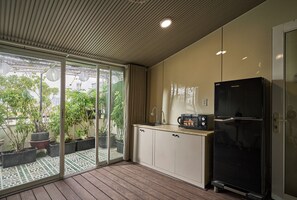 A modern kitchen with a black refrigerator, a microwave, and a sink. There is a sliding glass door leading to a patio with potted plants. - Maison Truong Thinh Hotel by Urban B (Ho Chi Minh City)