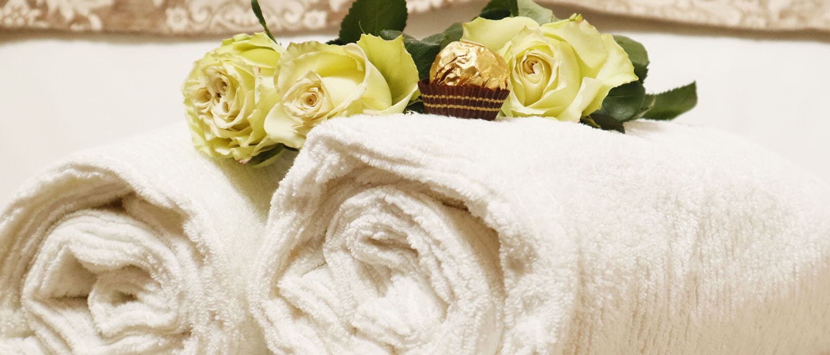 Neatly rolled white towels with a bouquet of yellow roses and a chocolate-covered item on top.