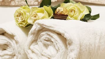 Neatly rolled white towels with a bouquet of yellow roses and a chocolate-covered item on top.