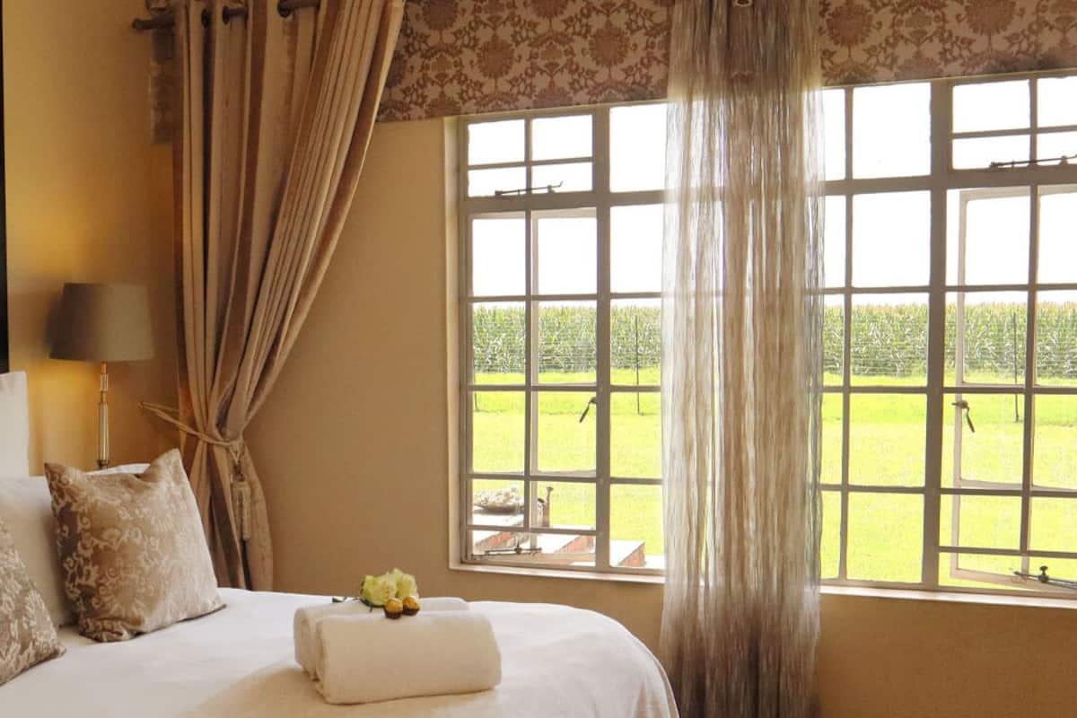 Een hotelkamer met een groot bed, een raam met uitzicht op een groen veld en een lampje op het nachtkastje.