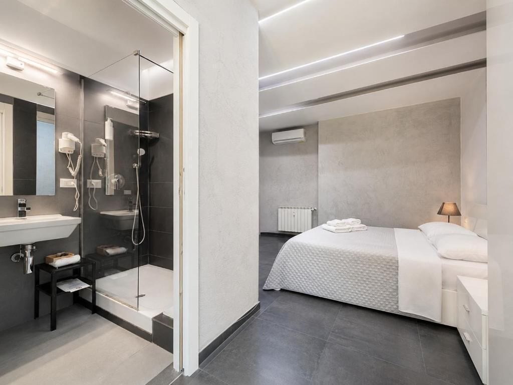 A modern bathroom with a glass-enclosed shower, a white sink, and a bed with a white bedspread.