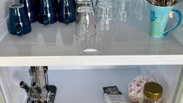 A kitchen shelf with various items including mugs, glasses, and a coffee machine.