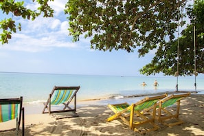 A beach with two wooden beach chairs under a tree, a clear sky, and calm sea. - Ban Na White Sand Beach (Ko Chang)