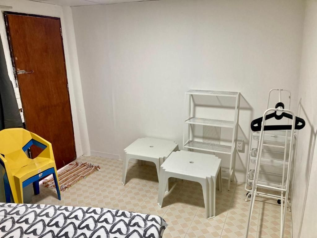A room with a bed, a yellow chair, two white tables, a white shelving unit, and a white ladder.