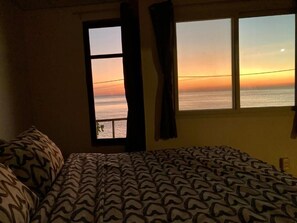 A bedroom with a bed, a window with curtains, and a view of the ocean at sunset. - Ban Na White Sand Beach (Ko Chang)