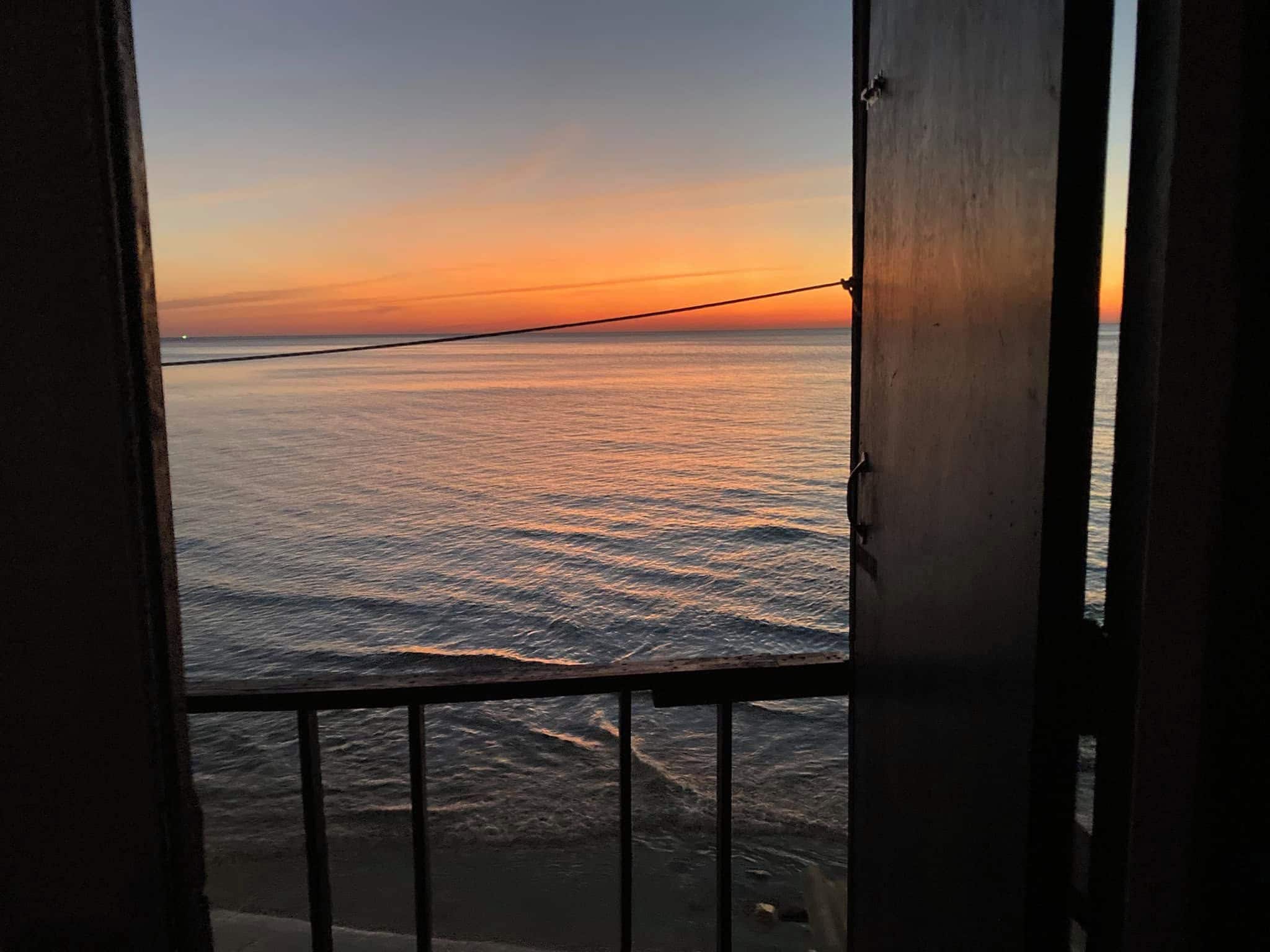 Vista al mar a través de una ventana con barandilla metálica.