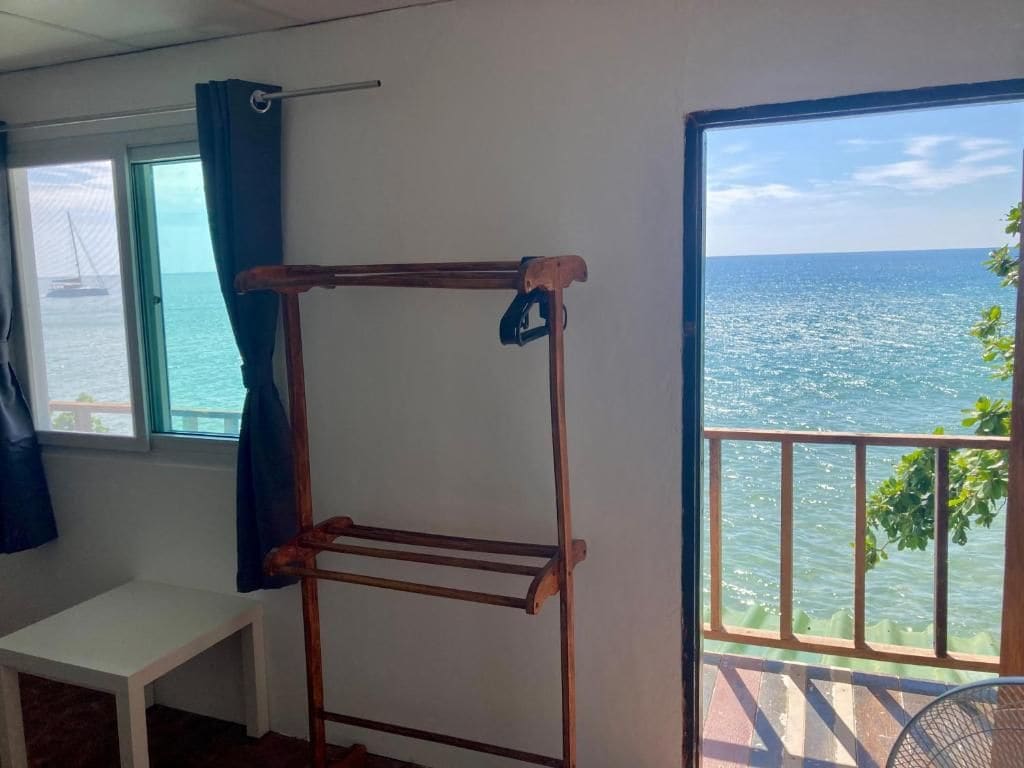 A room with a metal drying rack, a small table, and a view of the sea through a balcony door.