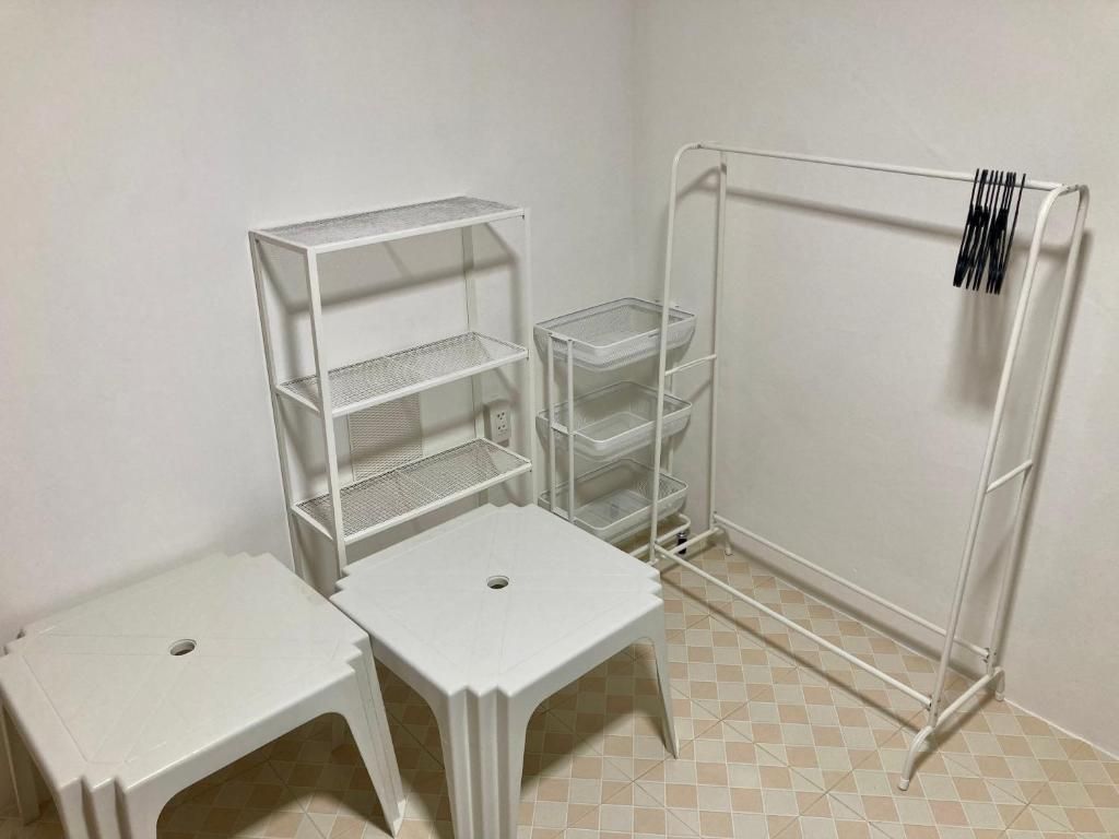 A room with a white metal shelving unit, two white stools, and a white metal rack with a barcode.