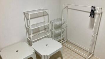 A room with a white metal shelving unit, two white stools, and a white metal rack with a barcode.