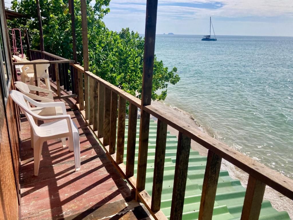 A wooden deck with chairs overlooking a calm sea, a sailboat in the distance, and a clear sky.