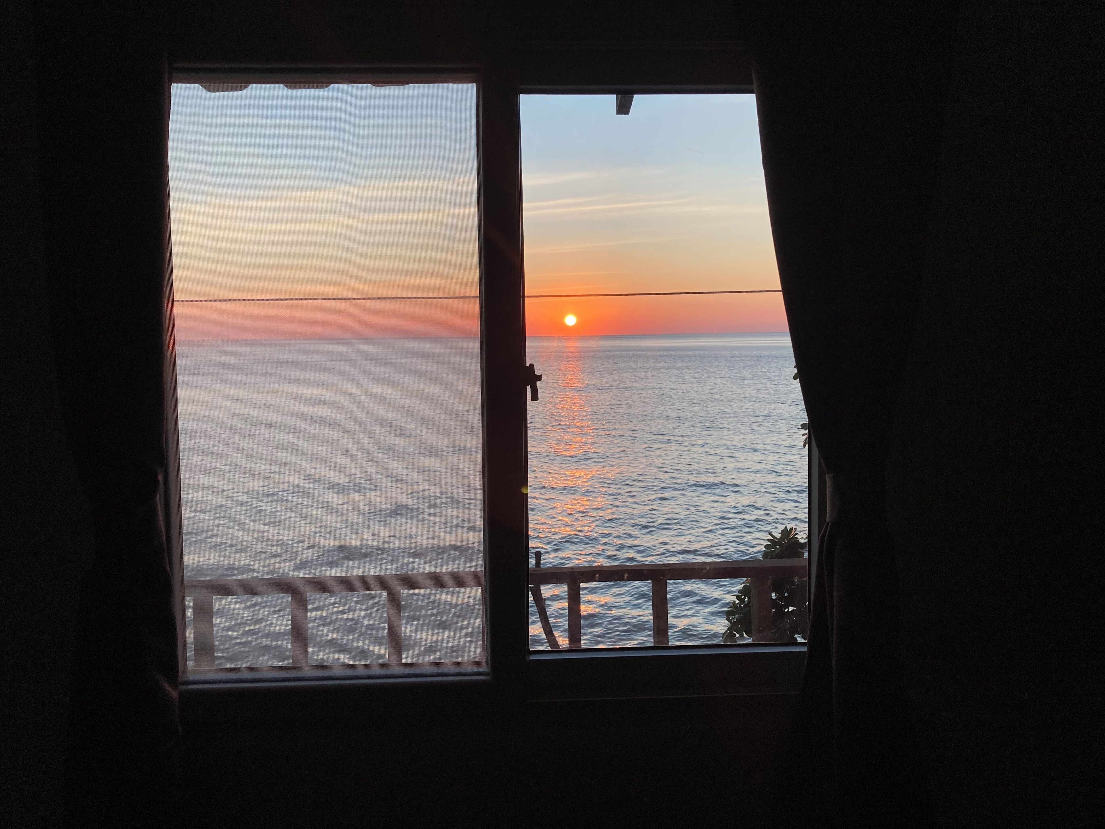 A room with a large window overlooking a body of water during sunset.