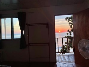 A room with a view of the sunset over the sea, a balcony with a railing, and a fan on the right. - Ban Na White Sand Beach (Ko Chang)