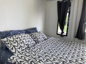 A bed with patterned bedding, a window with curtains, and a view of greenery outside. - Ban Na White Sand Beach (Ko Chang)