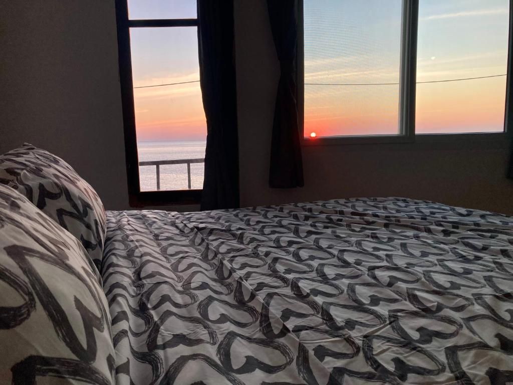 A bed with a patterned bedspread, a window with curtains, and a view of the sunset.