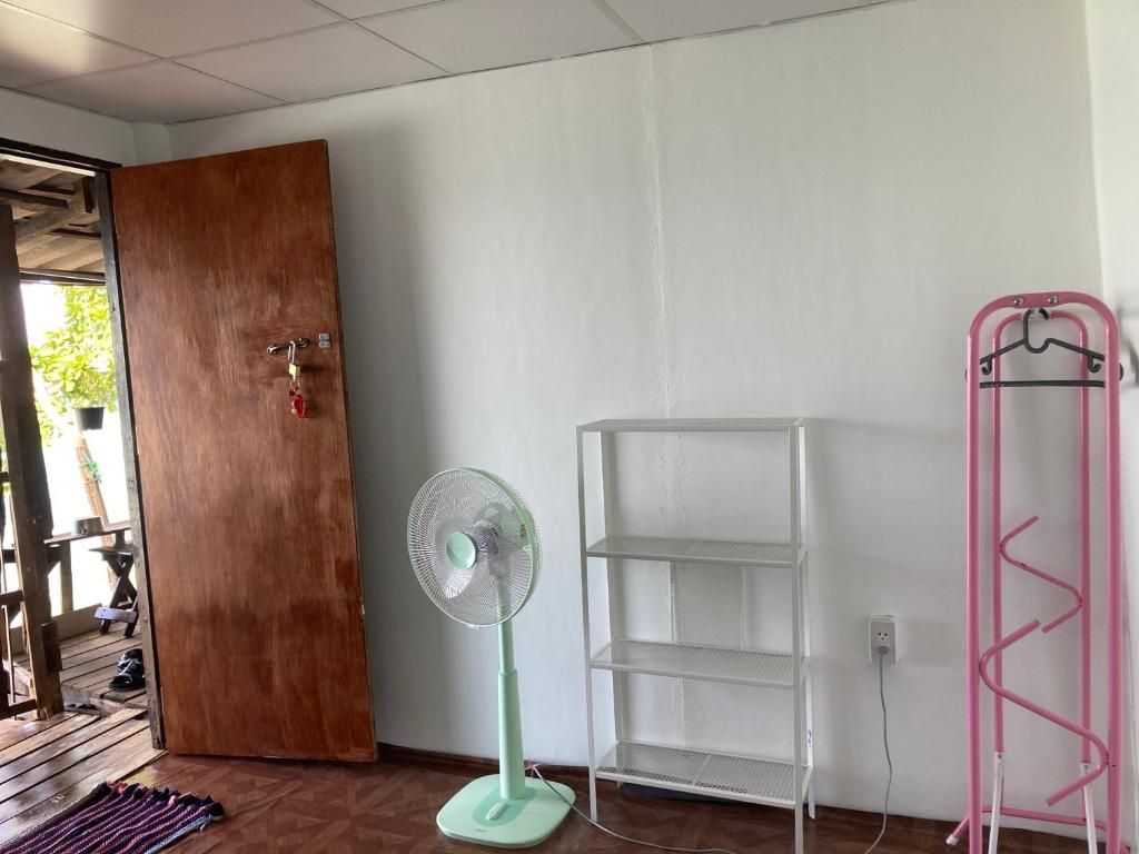 A room with a wooden door, a standing fan, a white metal shelf unit, and a pink hanger rack.