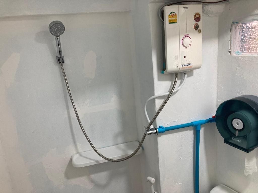 A shower with a handheld showerhead, a control panel, and a towel dispenser.