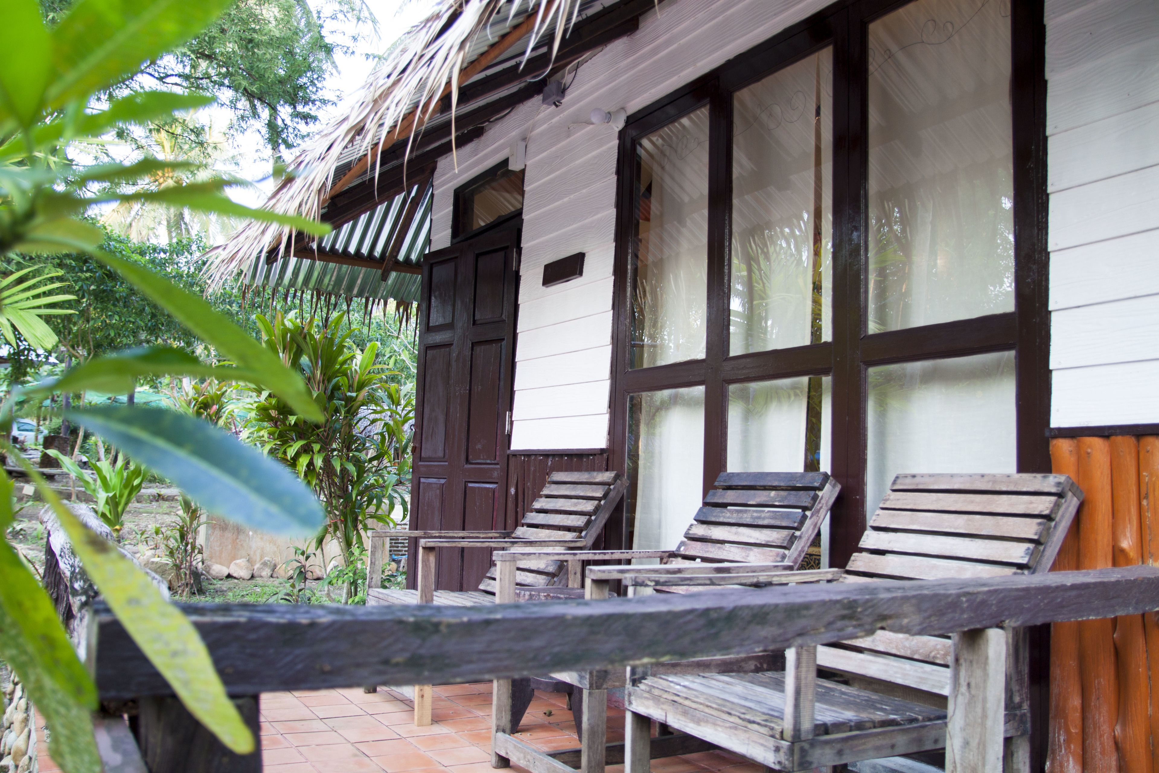 A wooden deck with lounge chairs, a thatched roof, and large windows overlooking a garden.