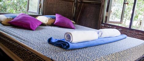 Una habitación con una cama con una colcha estampada, varias almohadas y toallas enrolladas.