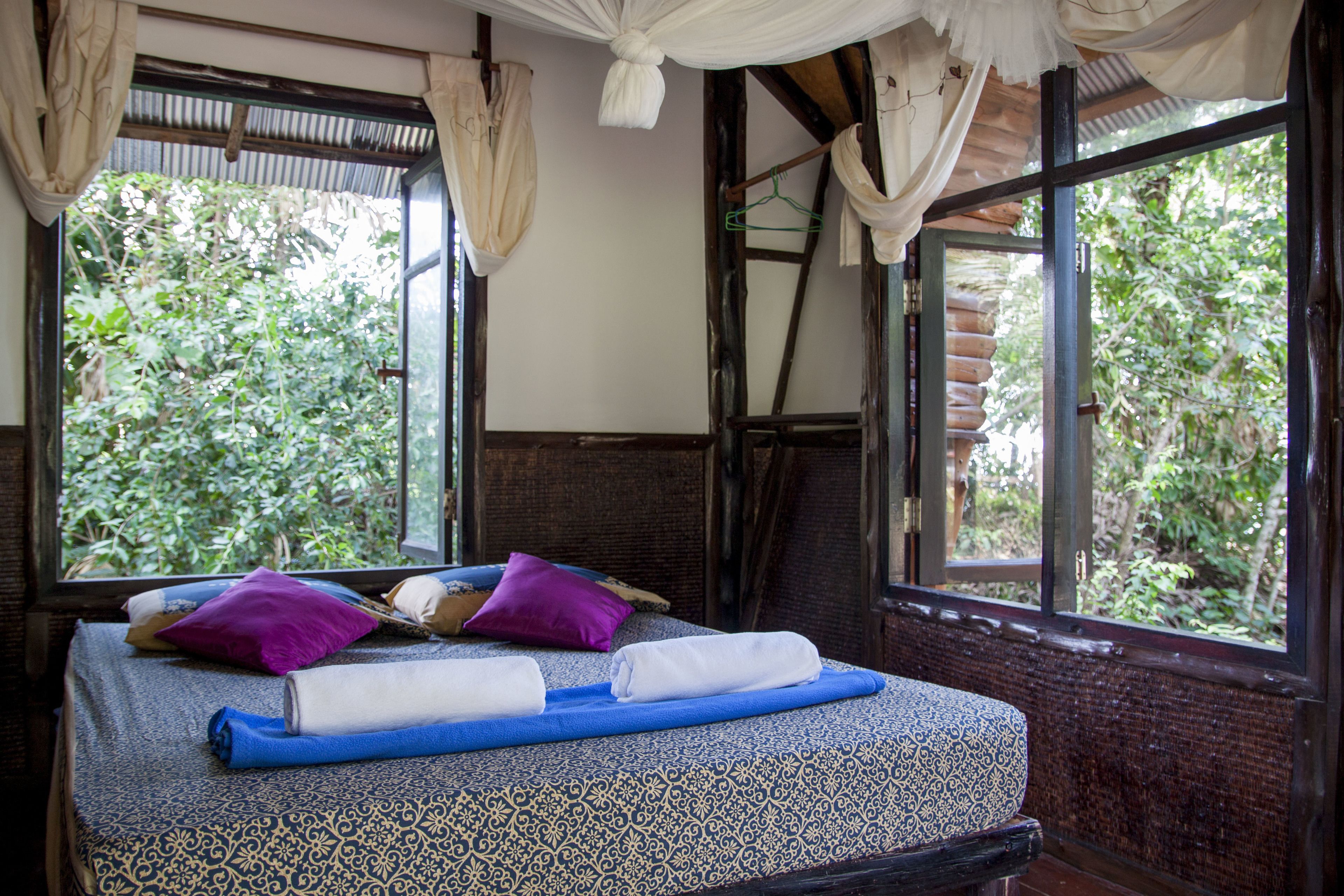 A bed with a patterned bedspread, two pillows, and a rolled towel.
