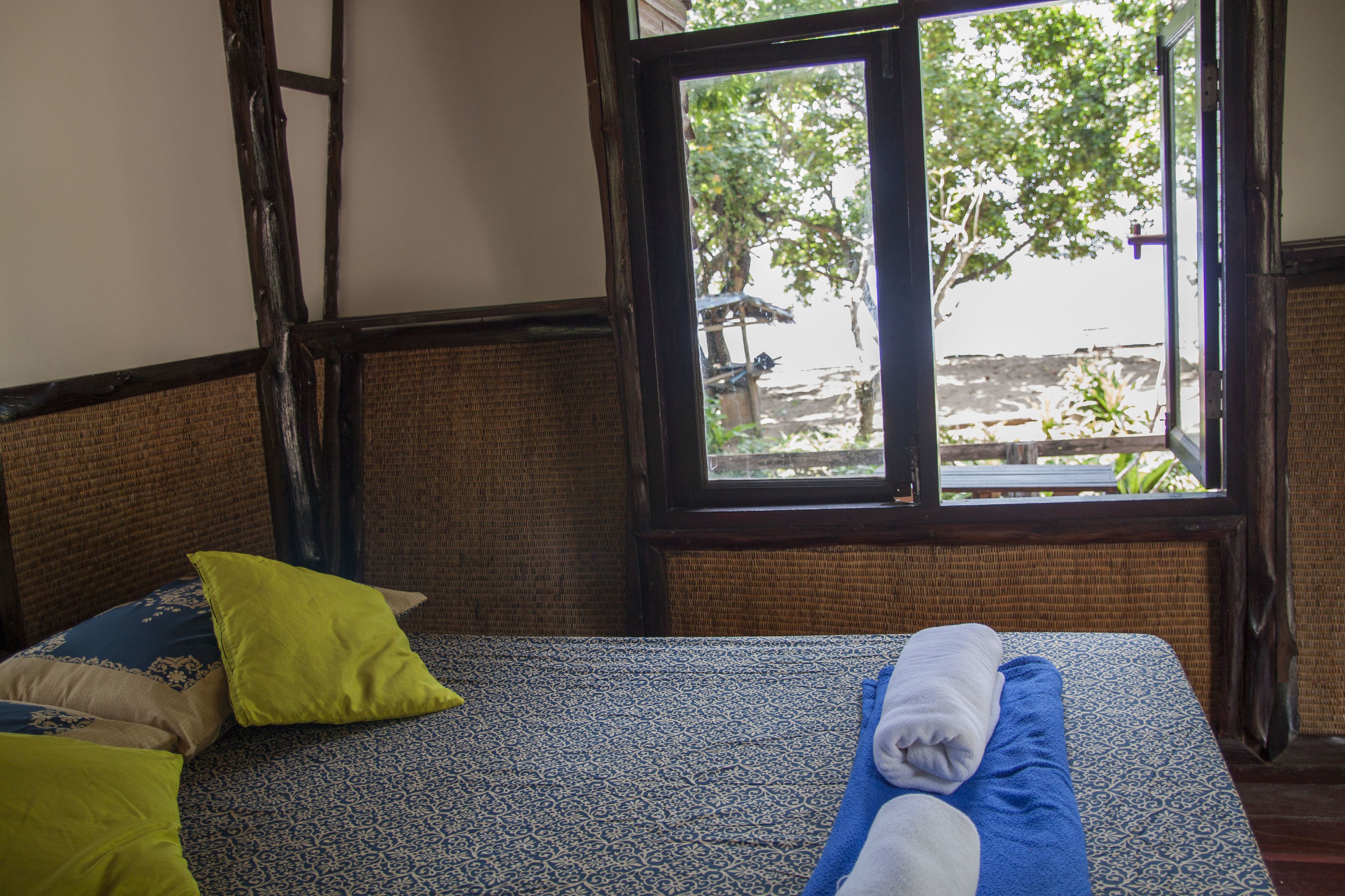 Ein Zimmer mit Bett, Fenster und Blick auf Grün.