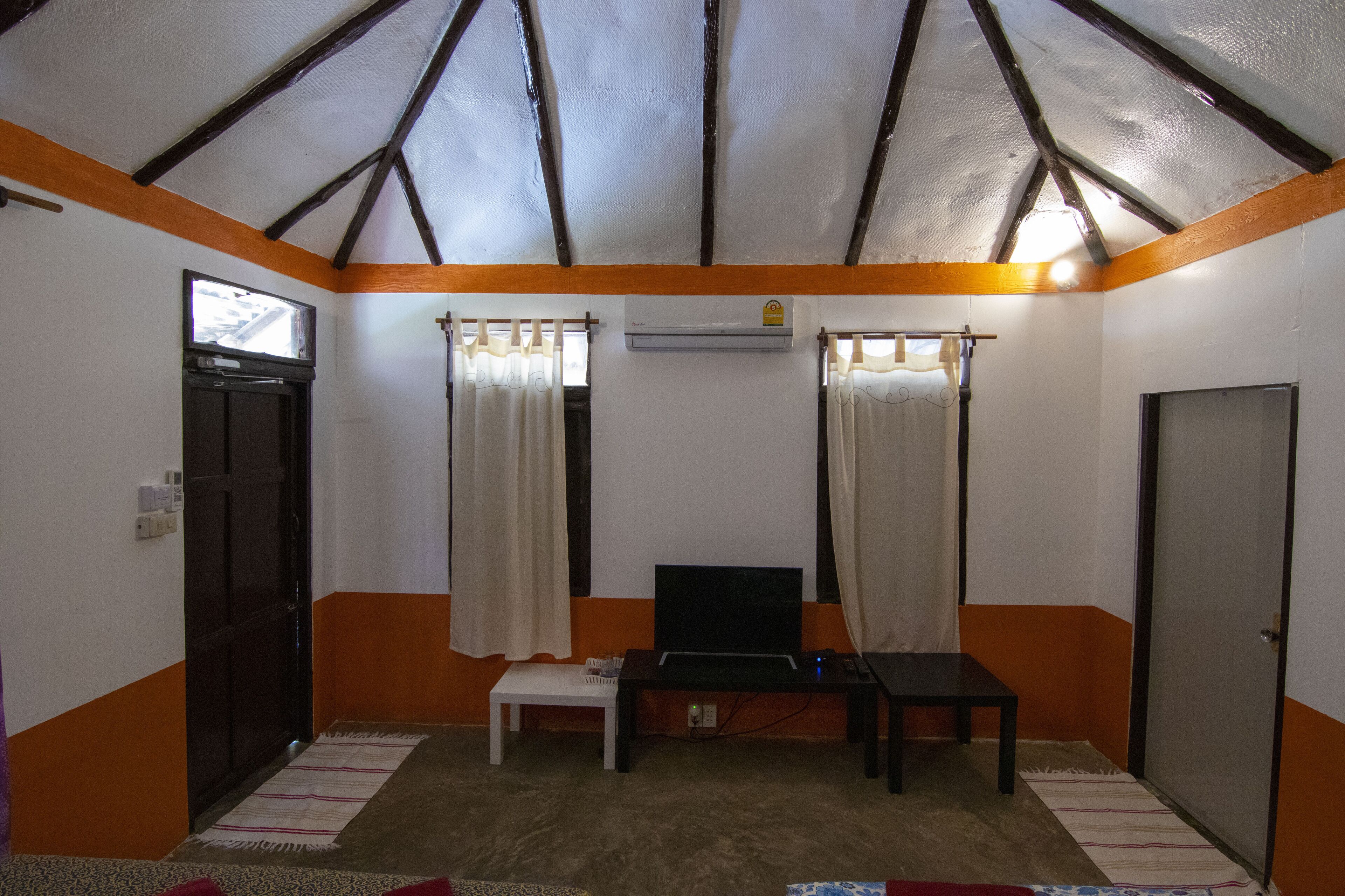 Una habitación con techo inclinado, una mesita, un televisor y cortinas.