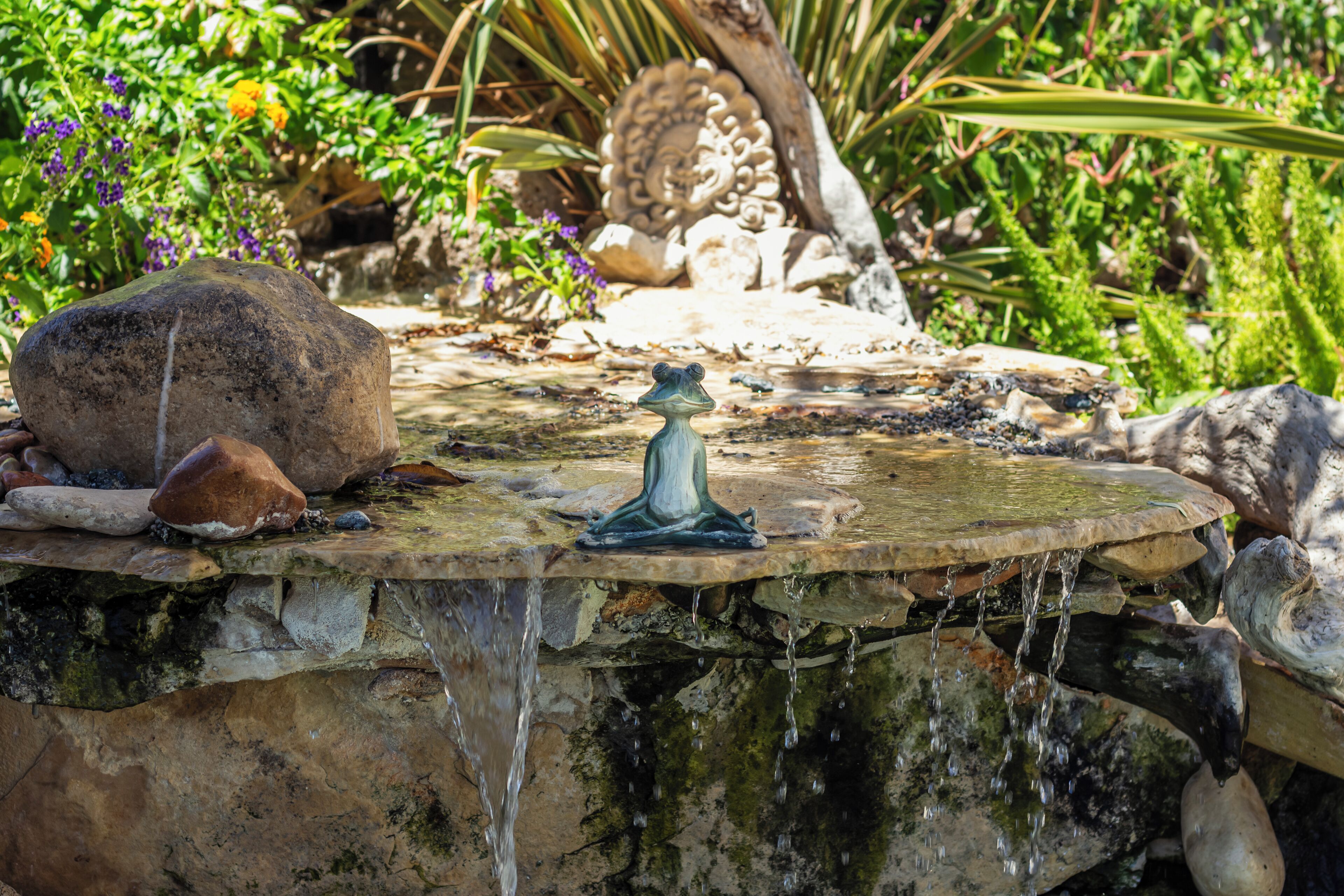 Una fuente de piedra con agua corriendo, rodeada de rocas y plantas.