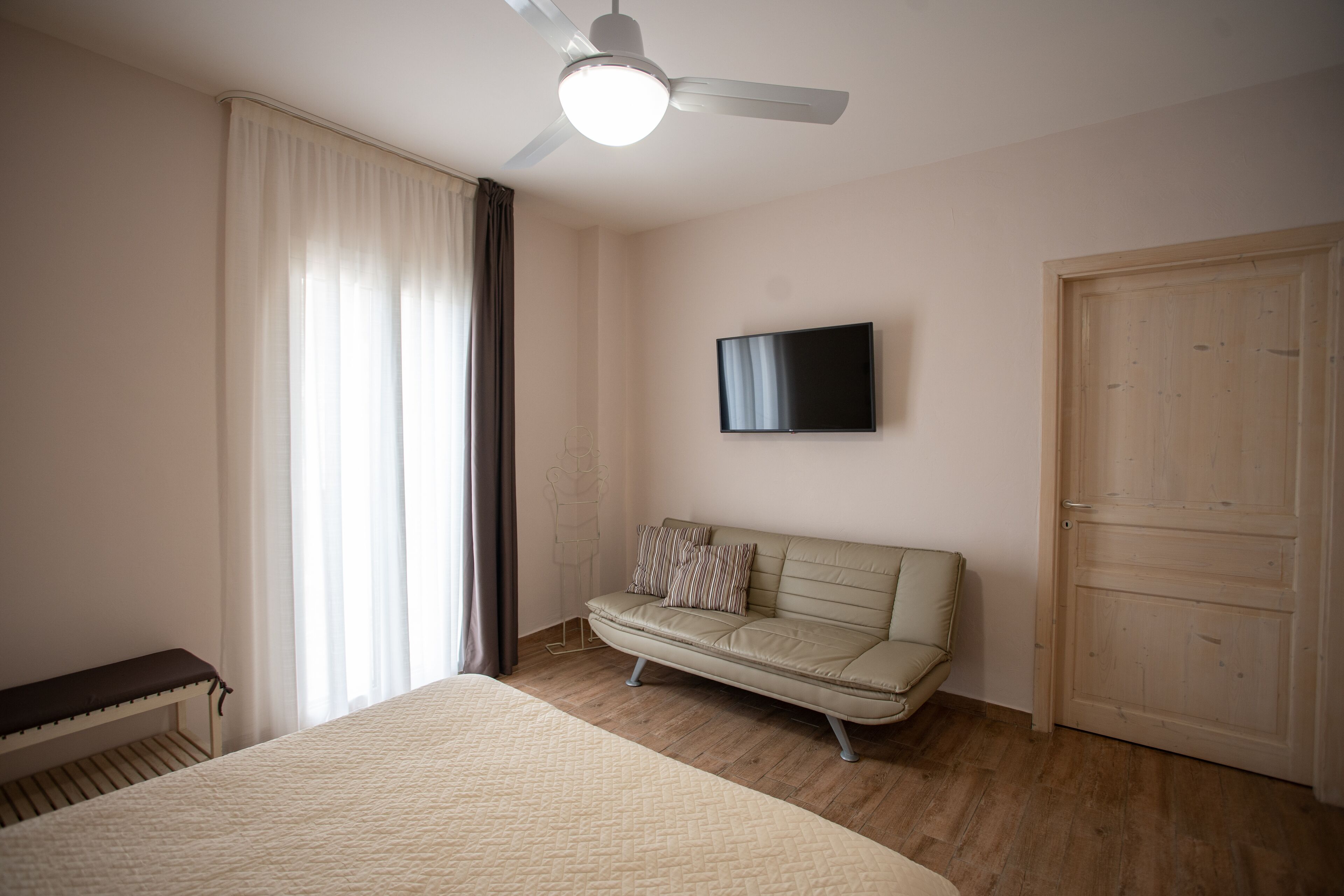 Una camera da letto con un letto, un divano, una ventola a soffitto, una TV e un armadio.