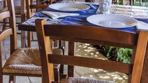 Un coin repas rustique avec des tables et des chaises en bois, un toit de chaume et des plantes suspendues.