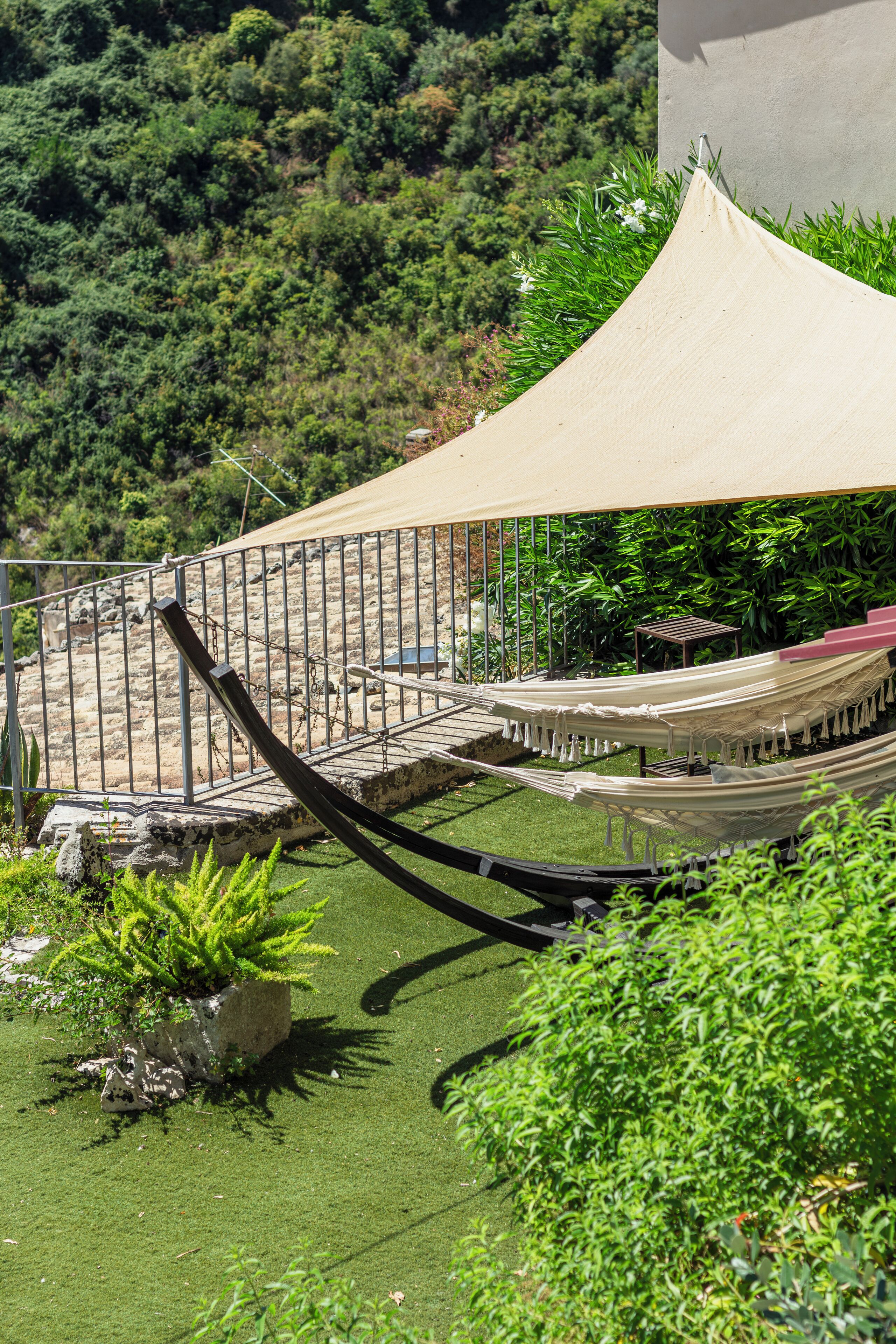 A hammock under a canopy, surrounded by greenery and a metal fence.