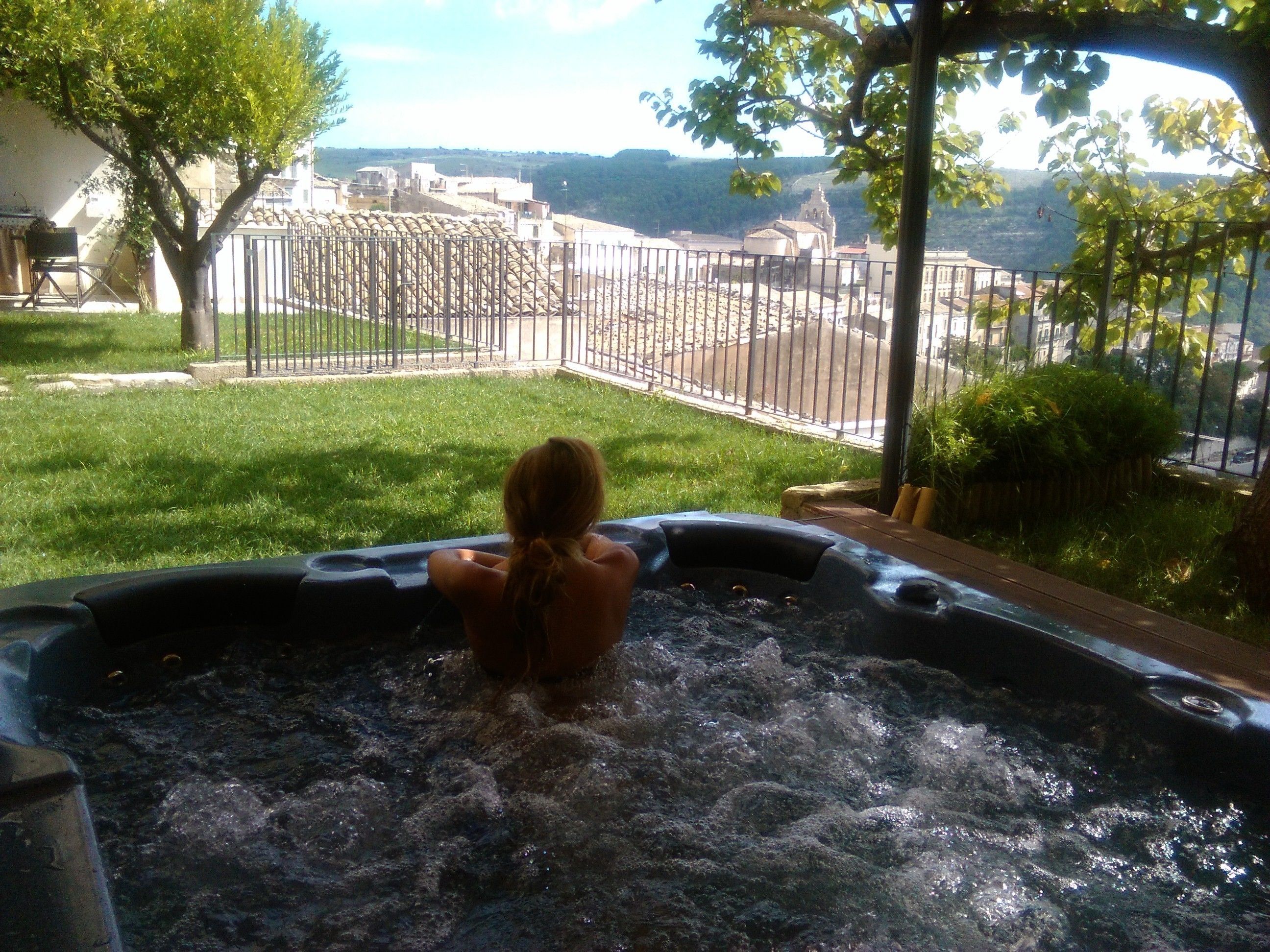Una persona in una vasca idromassaggio con vista su un panorama urbano e colline sullo sfondo.