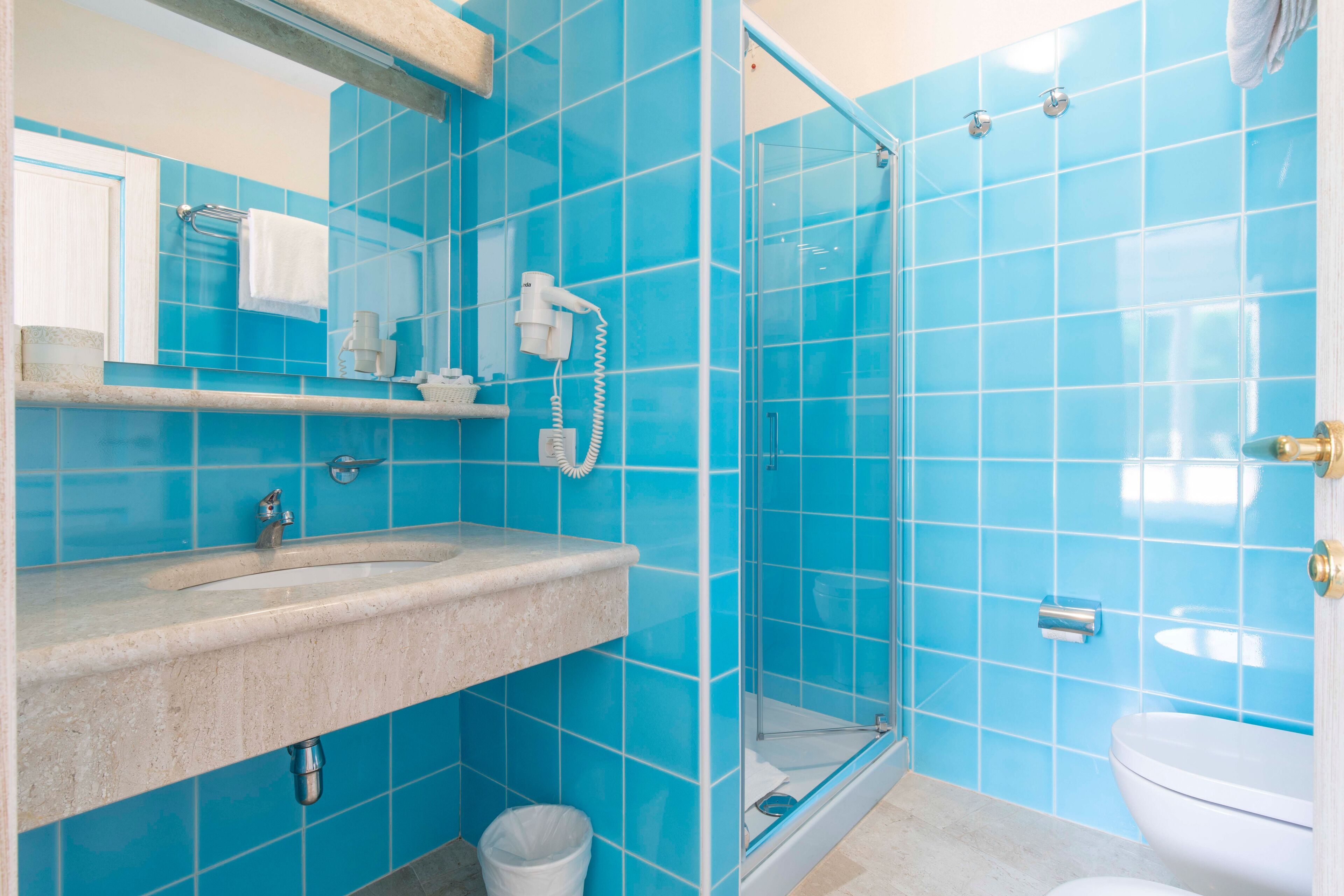 A bathroom with a sink, mirror, and a shower with blue tiles.