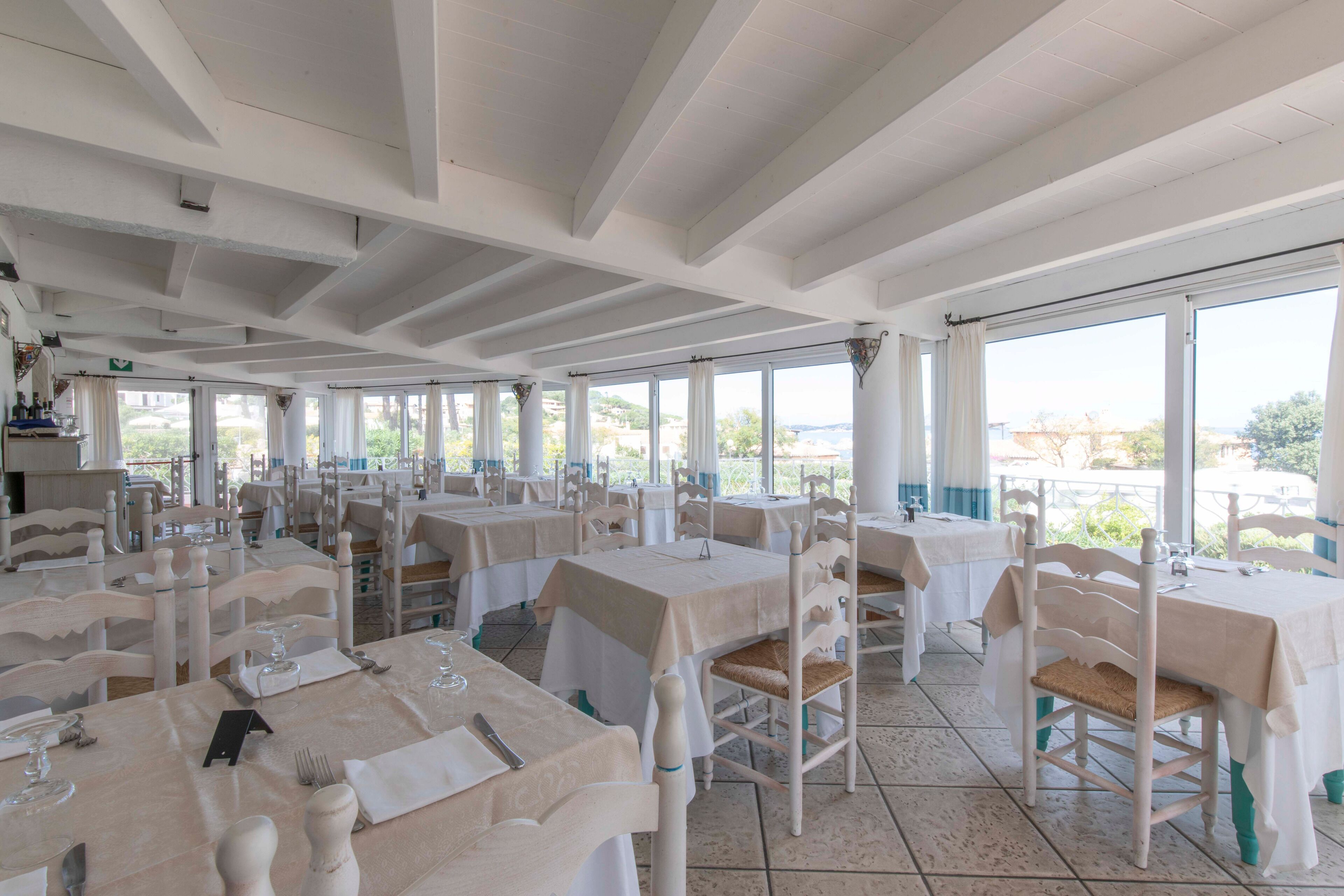 A restaurant with multiple tables and chairs, large windows, and a tiled floor.